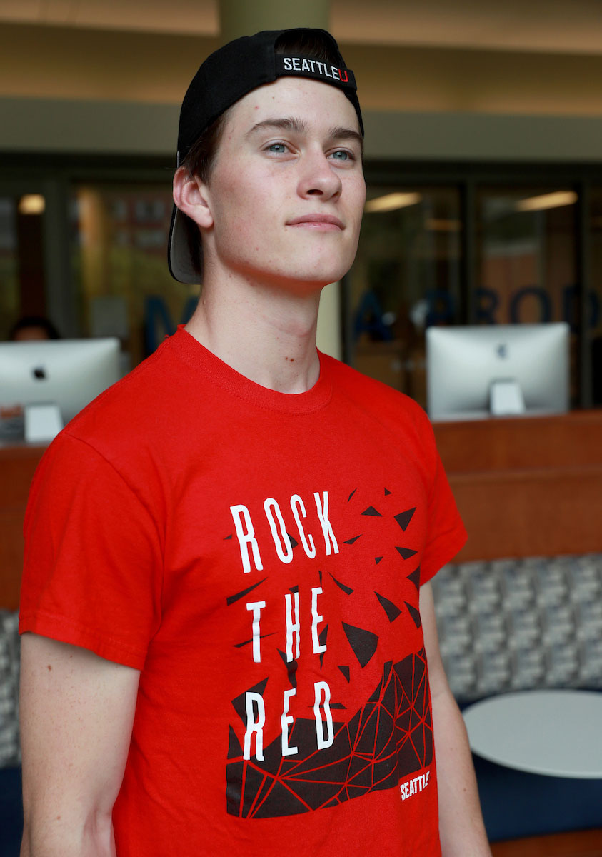 Student standing in the library computer lab wearing a branded 'Rock the Red' t-shirt